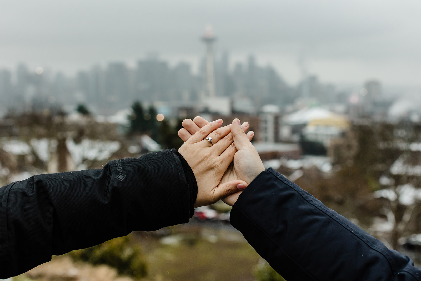 couple holding out hand with engagement ring and seattle skyline in the background on a cold winter day
