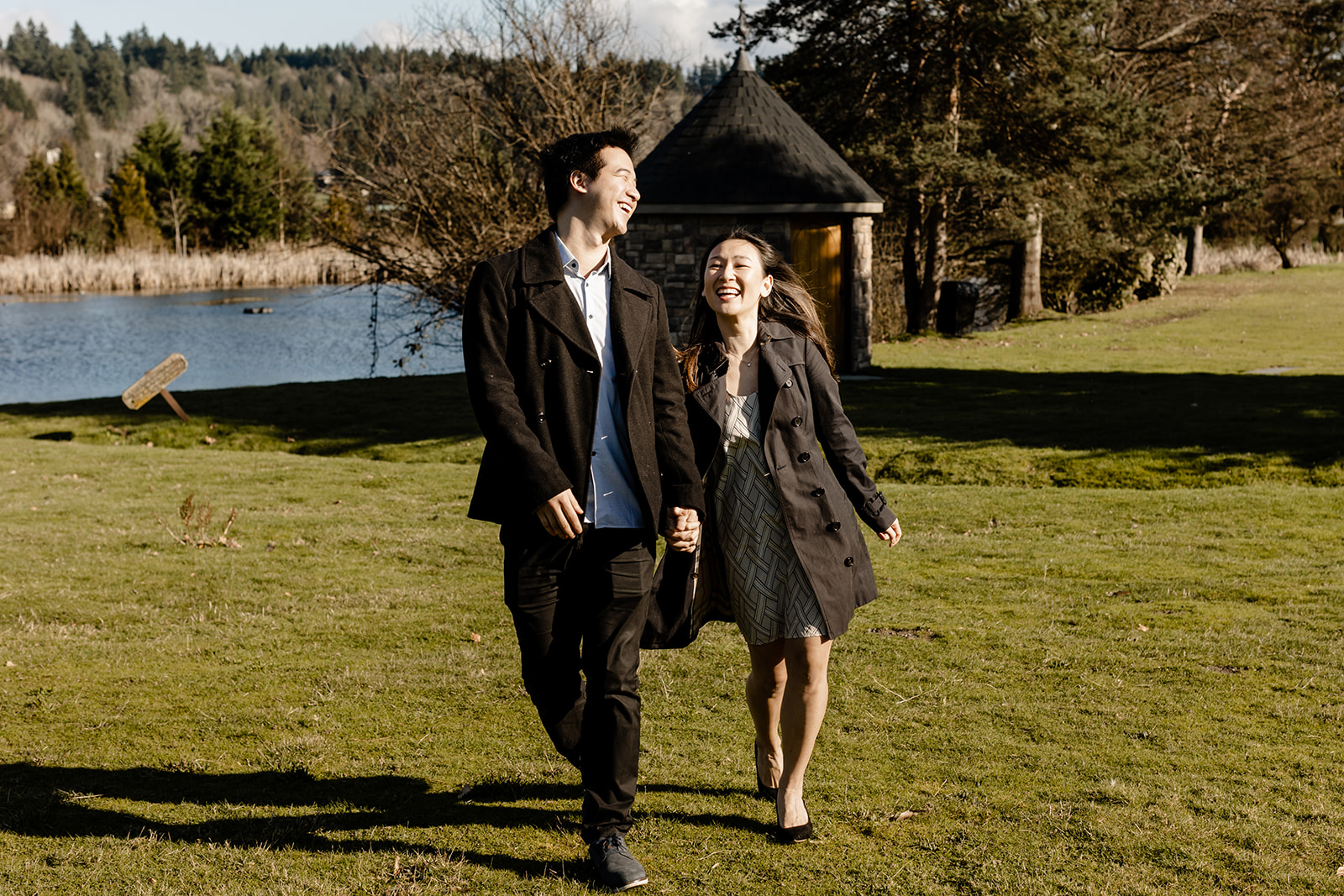 Couple at Chateau St. Michelle seattle proposal photographer holding hands walking toward camera with direct sunlight on faces as they smile and laugh