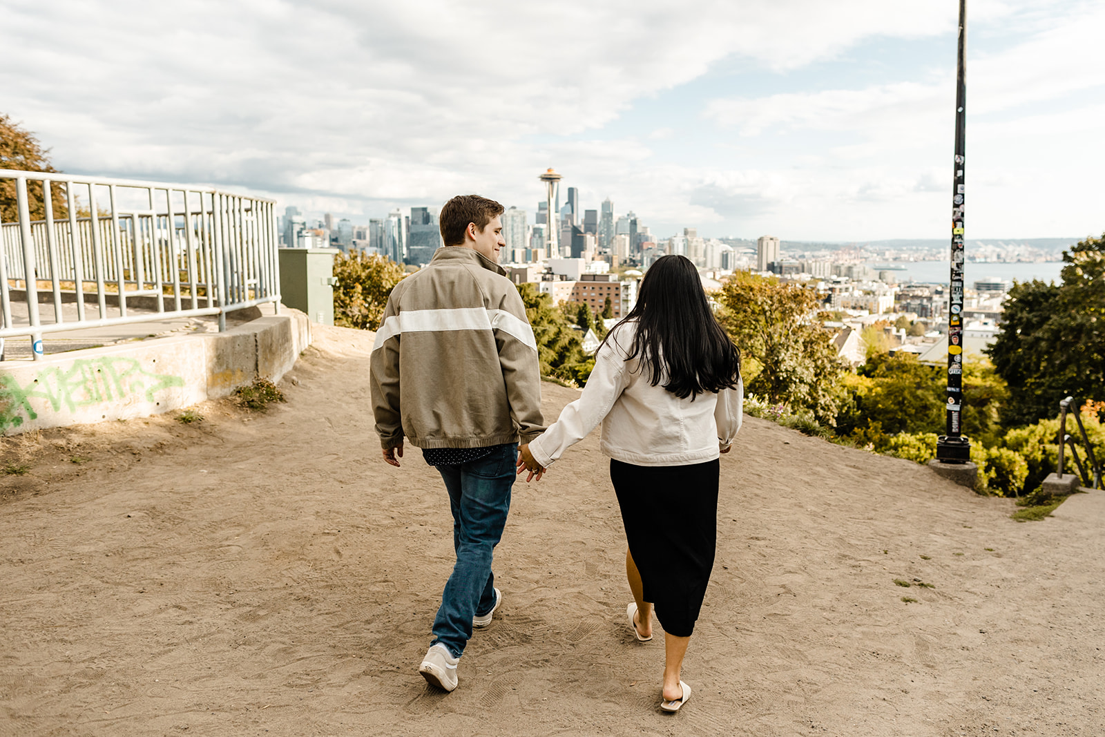 couple holding hands walking towards seattle skyline with space needle in background at Kerry park 