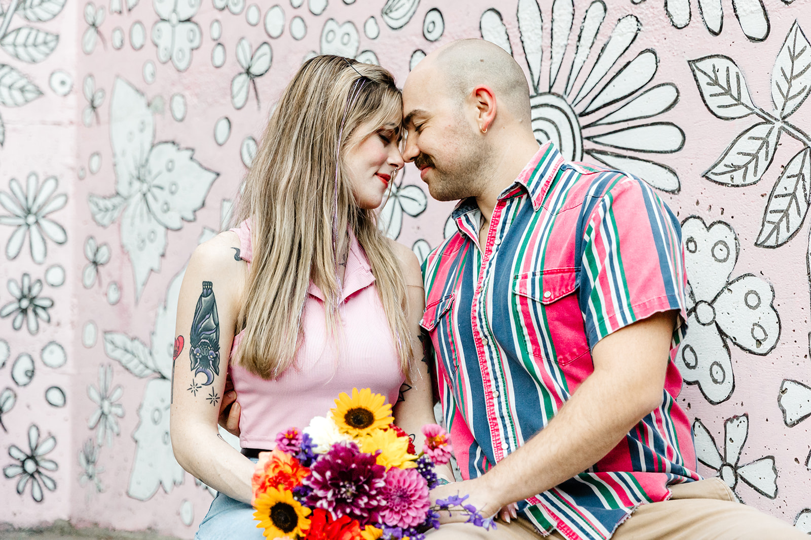 couple touching foreheads in front of pink floral wall