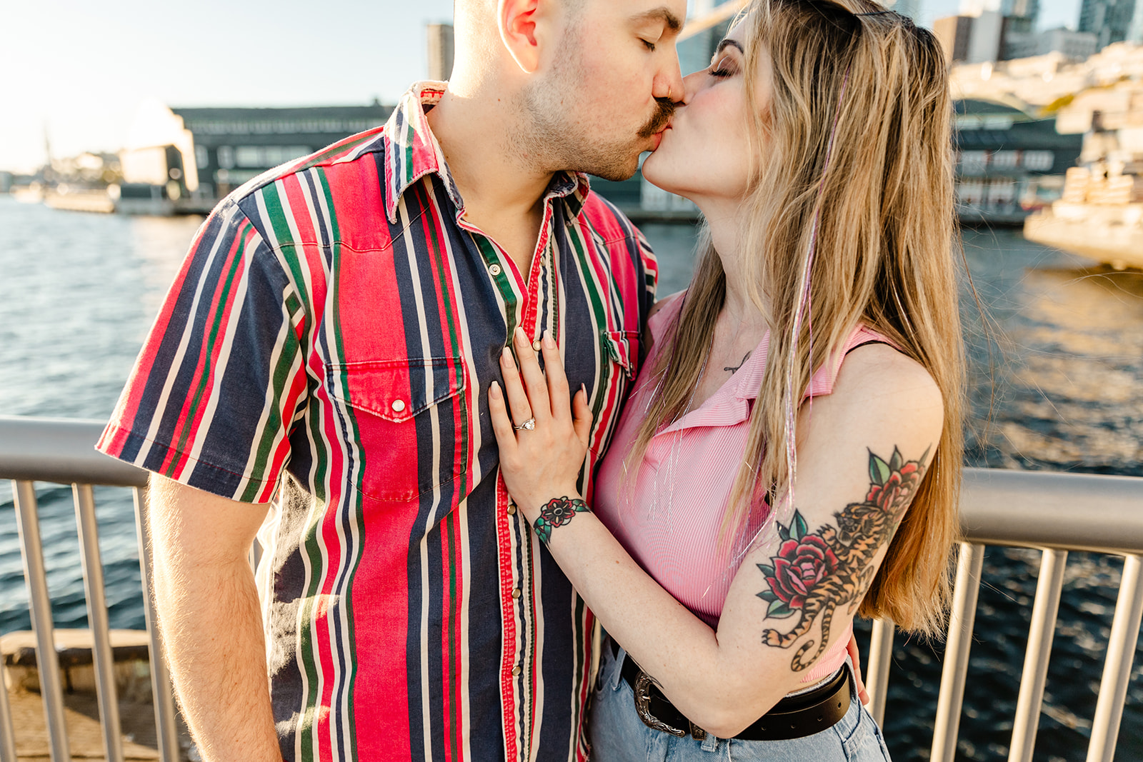 couple with vibrant color clothing kissing with woman hand on man chest showing off engagement ring, Seattle proposal photographer