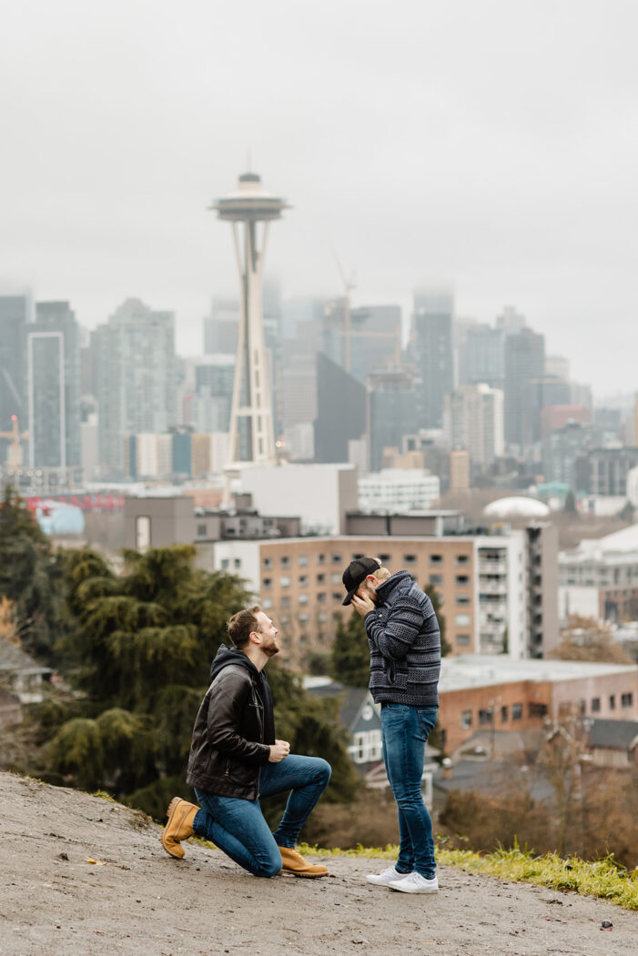 kerry park proposal photographer with space needle in background one man on one knee proposing to boyfriend with hands in face crying