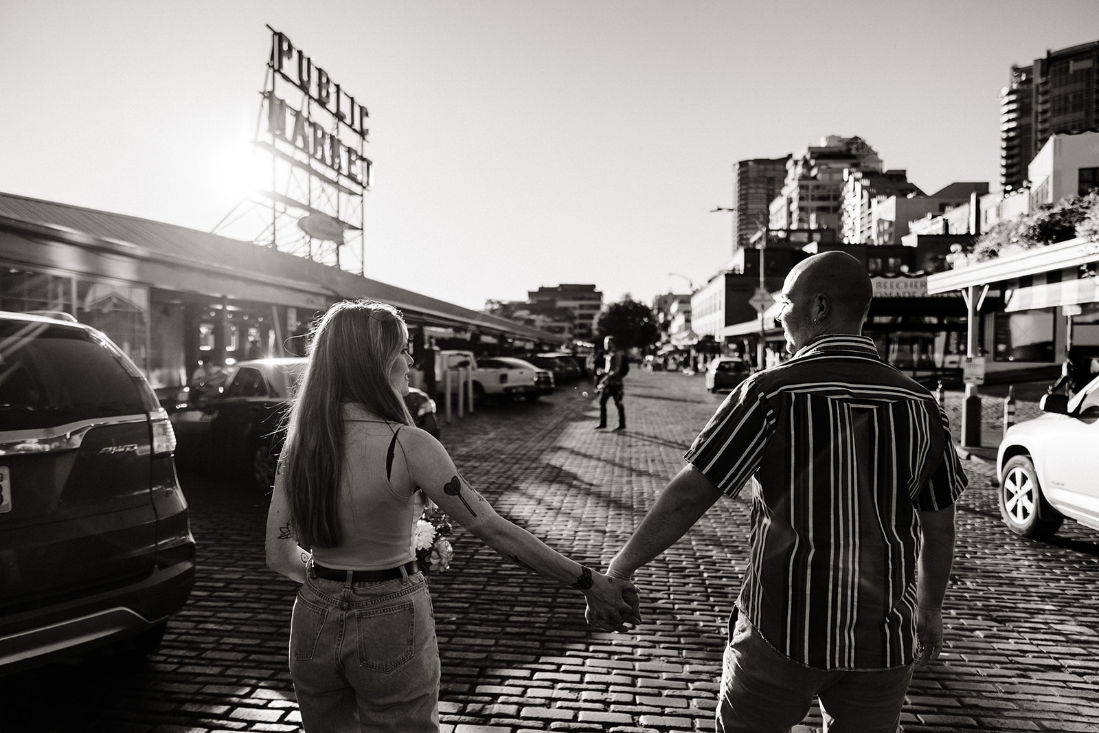 couple holding hands walking down pike place market together with people in the distance at sunset seattle proposal photographer