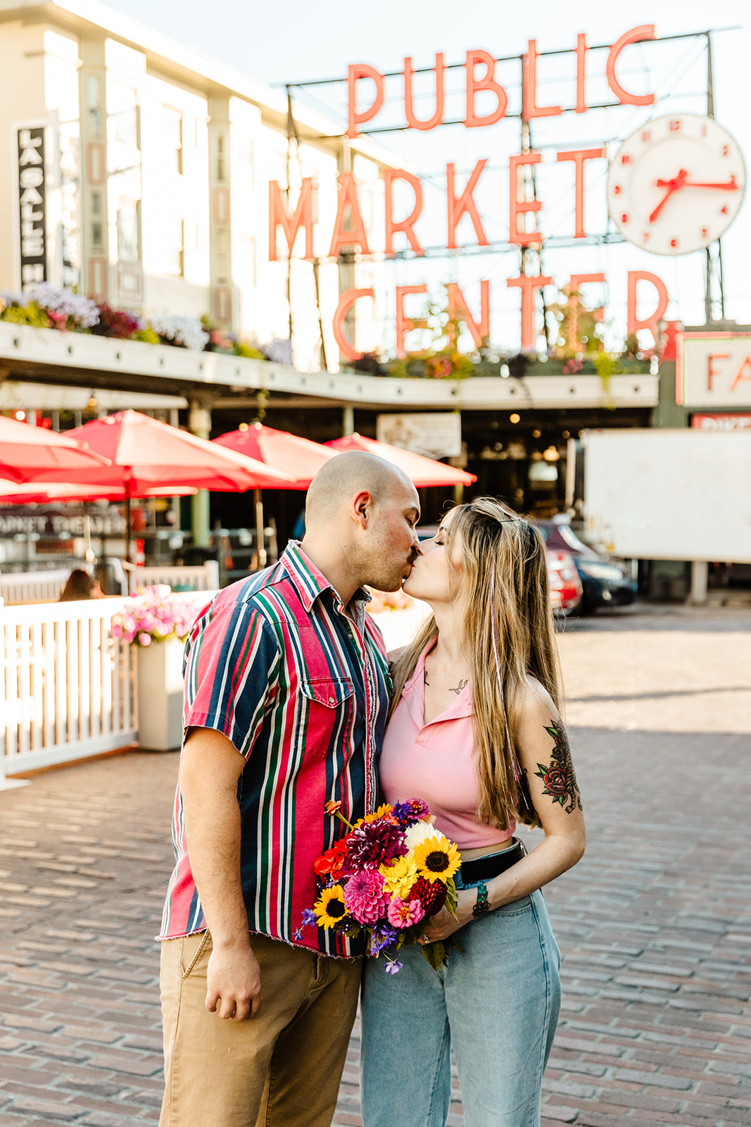 couple holding flowers kissing in front of pike place market center sign