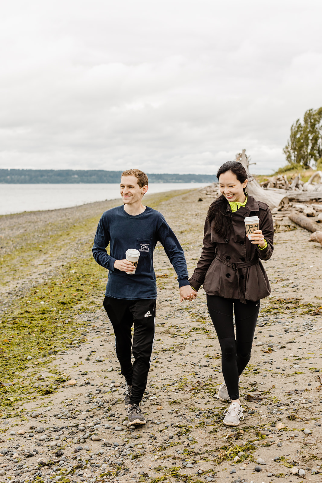 couple holding hands walking along the beach at discovery park holding Starbucks cups