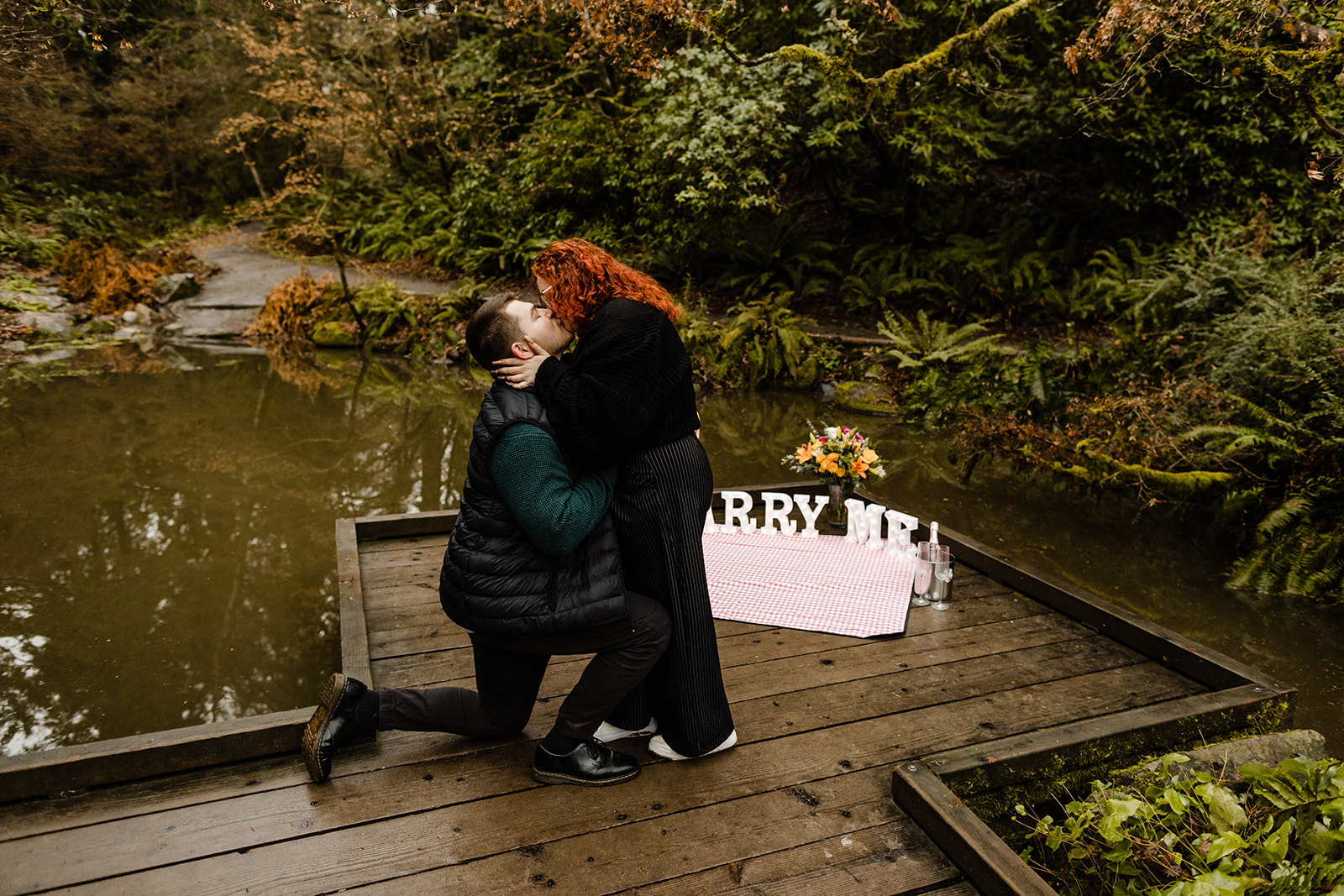 picnic proposal at seattle park, couple kisses with fiancé down on one knee