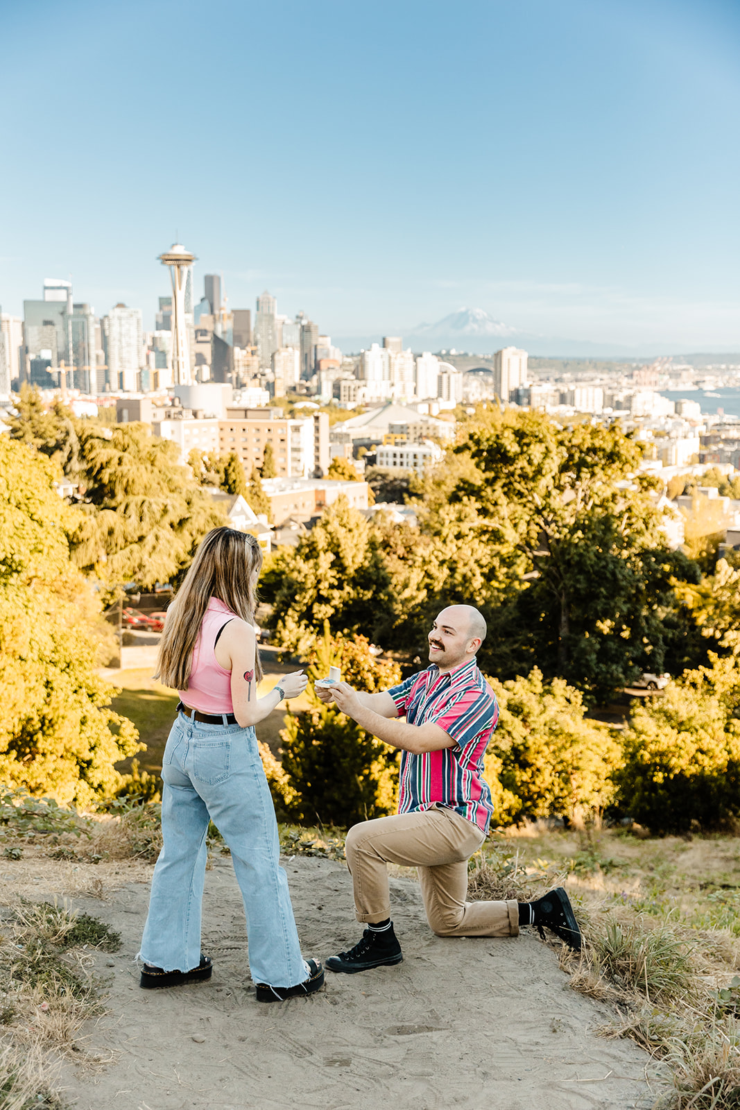 bright and colorful summer proposal at Kerry park with man on one knee in front of woman proposing