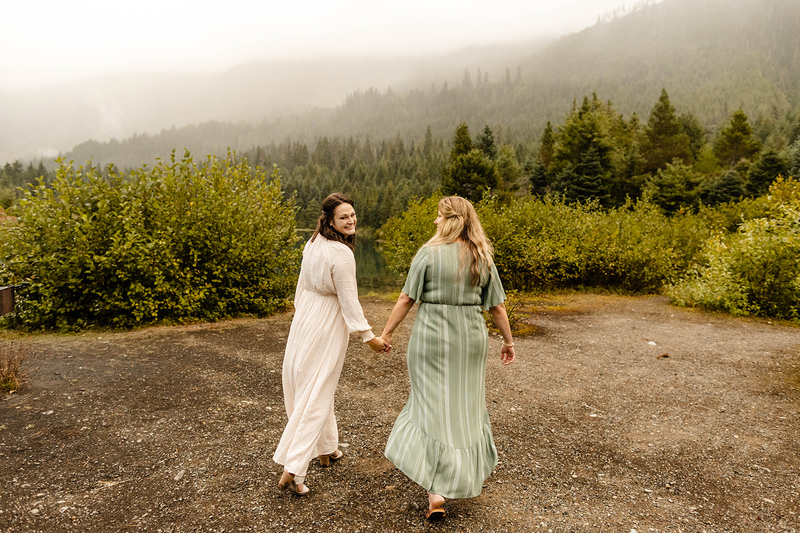 couple walks away from the camera, partner on the left looking over her shoulder and smiling at the camera