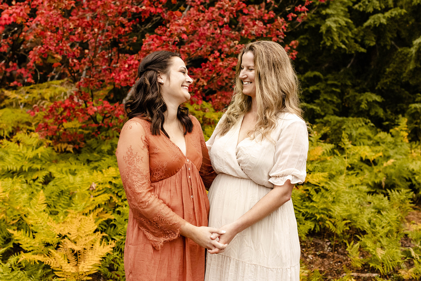 couple hold hands and smile at each other for their fall engagement photos