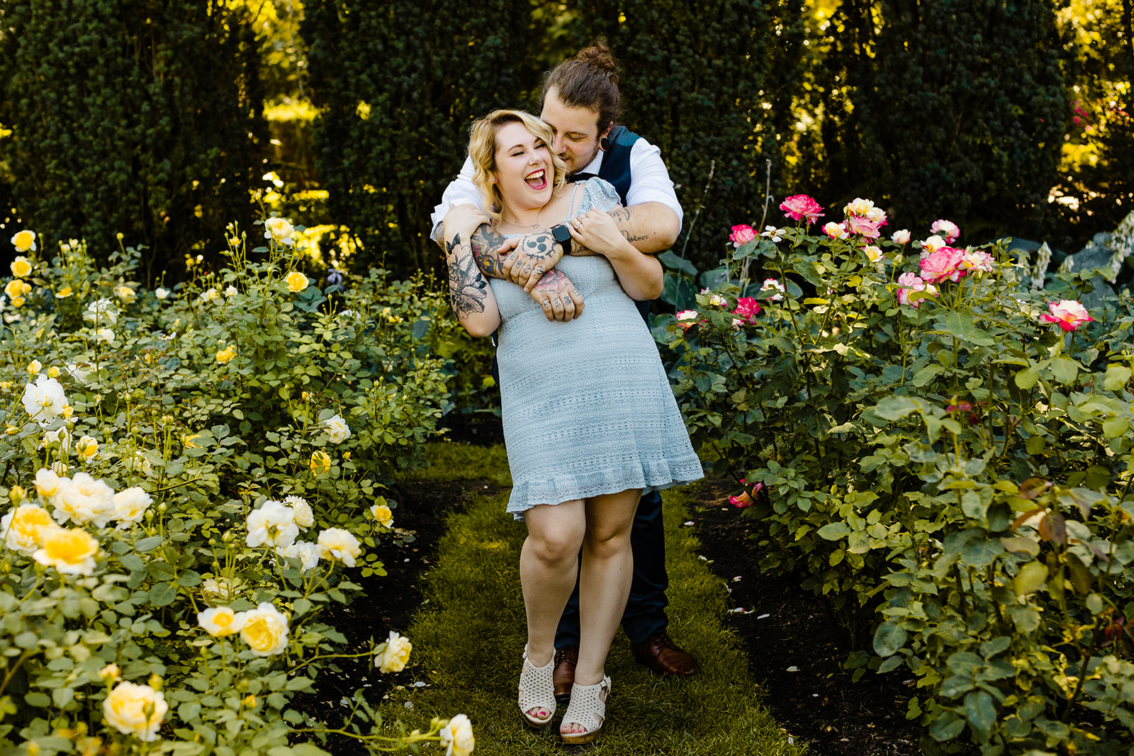 a blog post about What to wear for my engagement session and photos of lots of outfits to support the idea. Light blue lace dress woman being hugged from behind by her fiancé in the portland rose garden after proposal
