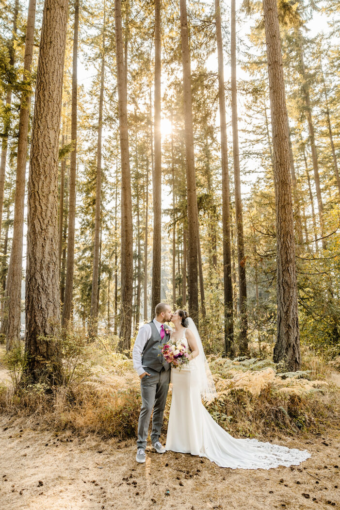 woodsy wedding with sunlight pouring through trees, couple standing side by side kissing