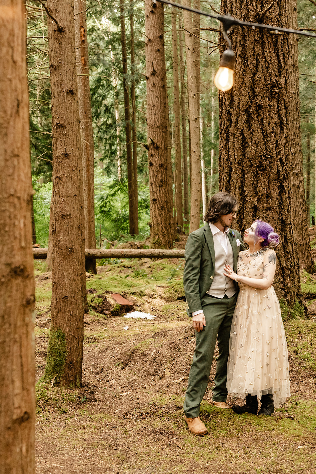 Couple smiles at each other during portraits in the forest.