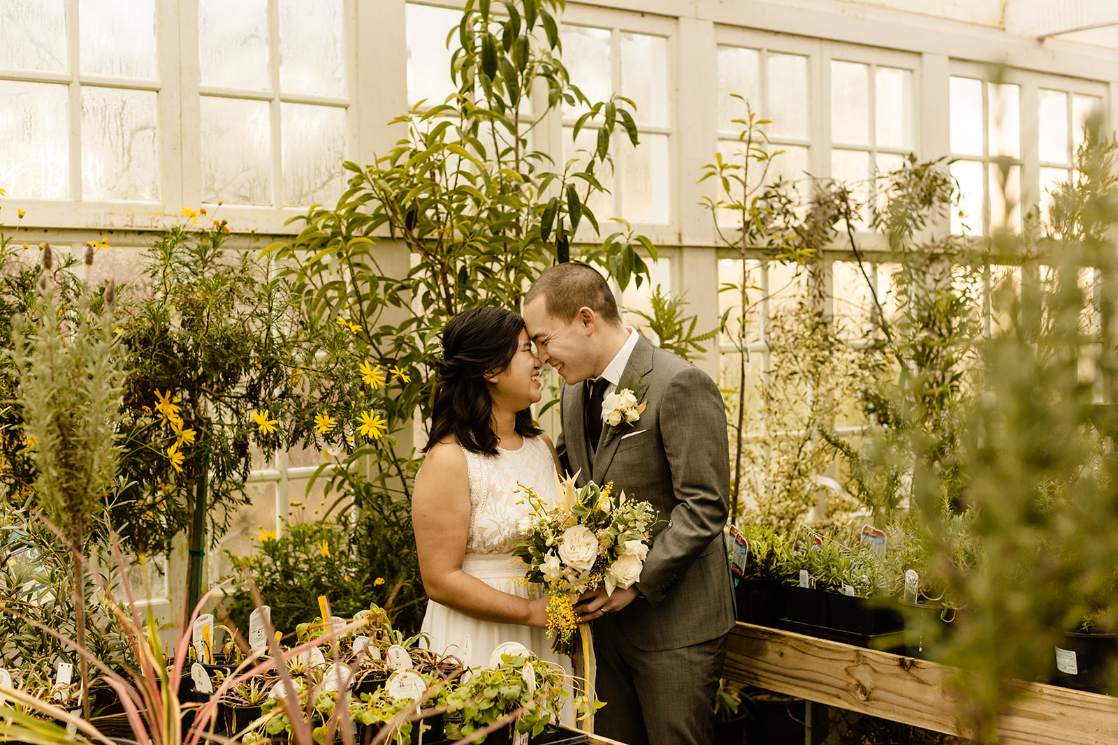 A greenery inspired wedding theme: couple takes portraits in a greenhouse surrounded by plants.