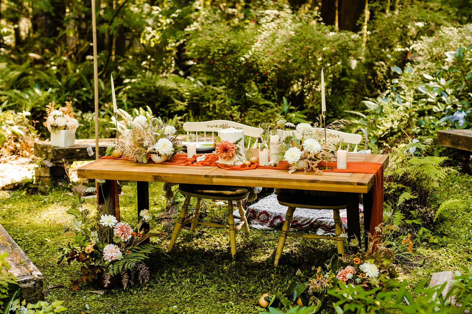 A greenery inspired wedding theme reception table showing white florals, orange accents, and a lush outdoor setting.
