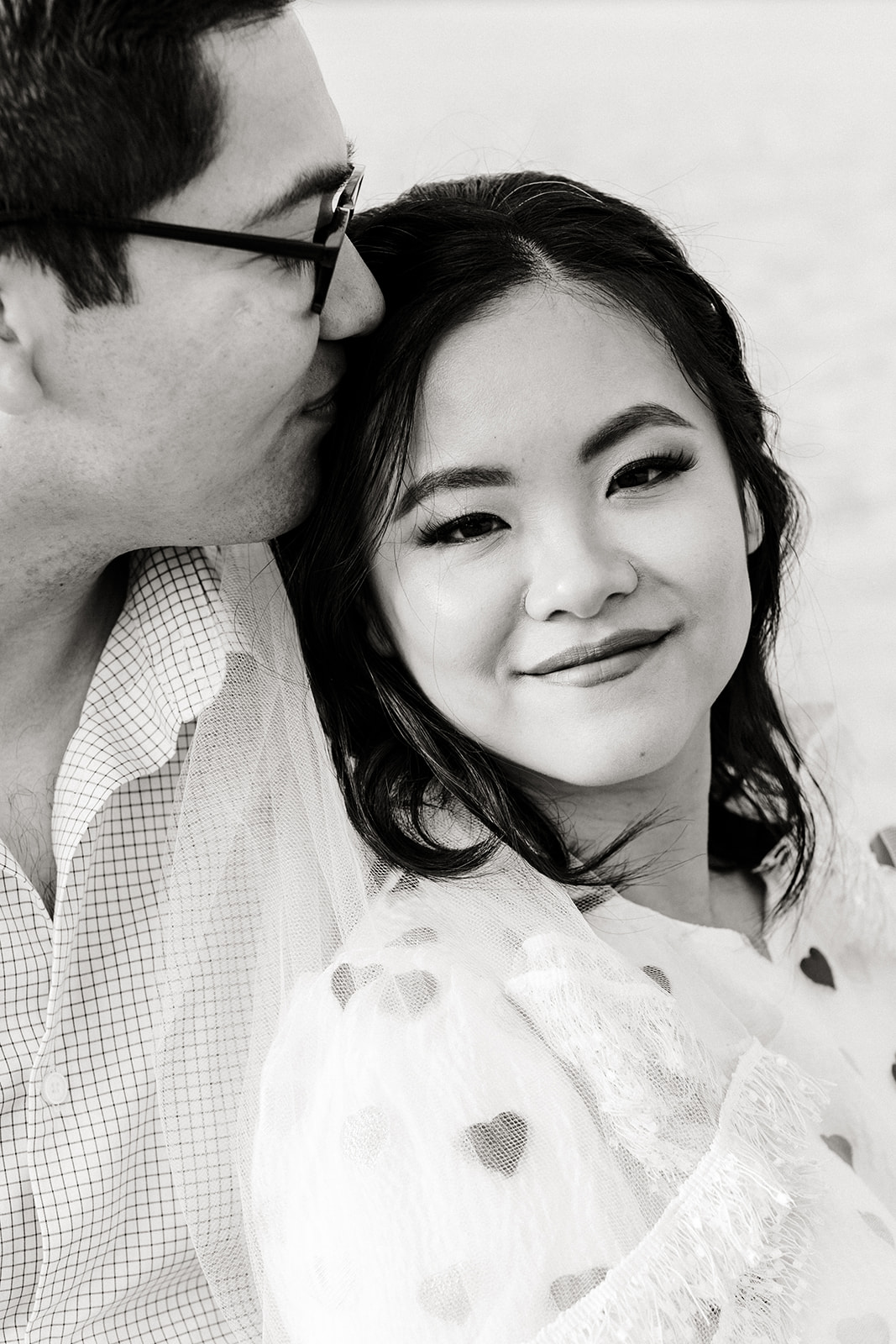 Groom kisses bride on the temple, black and white. 