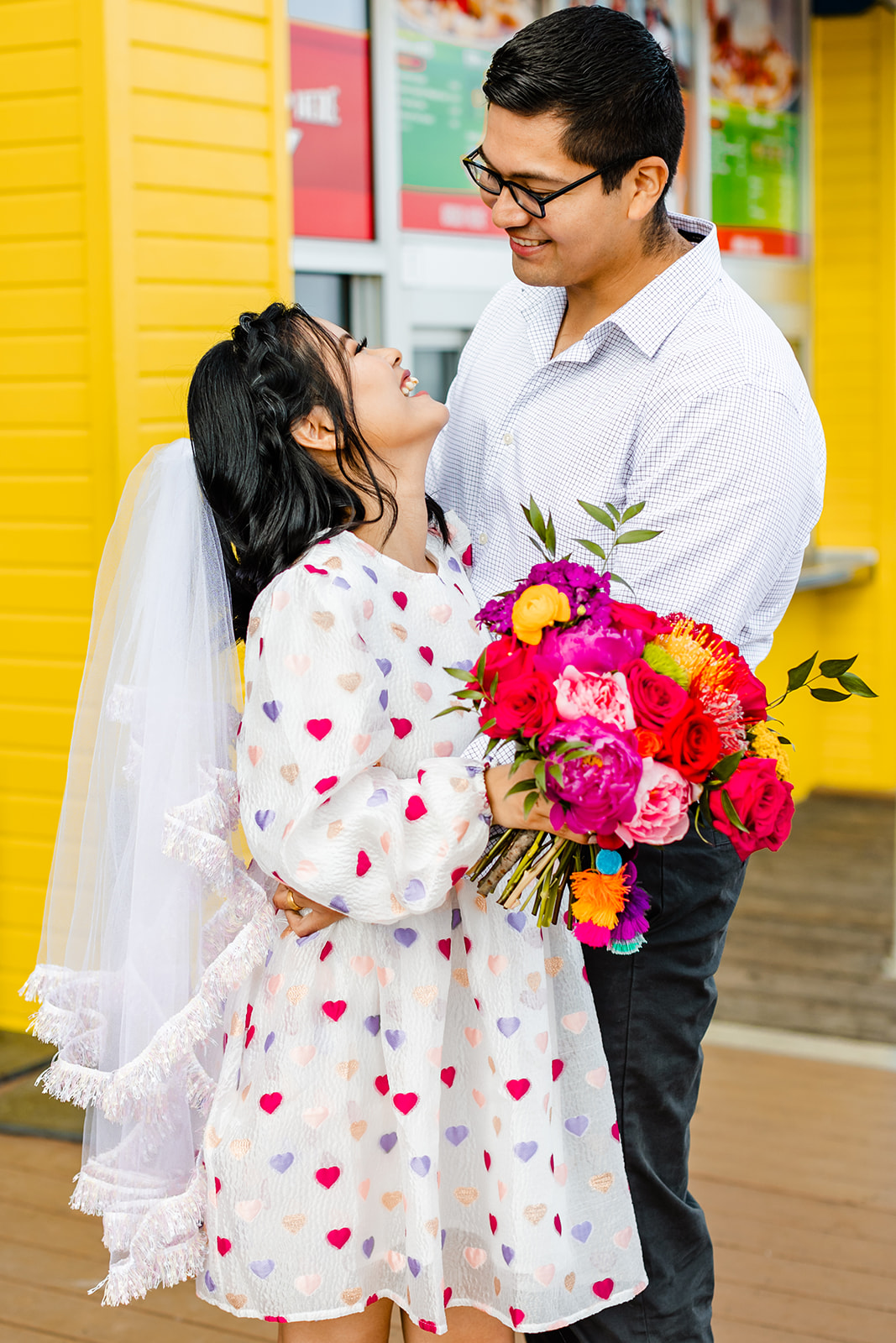 Bride smiles up at groom, holding colorful bouquet. 
