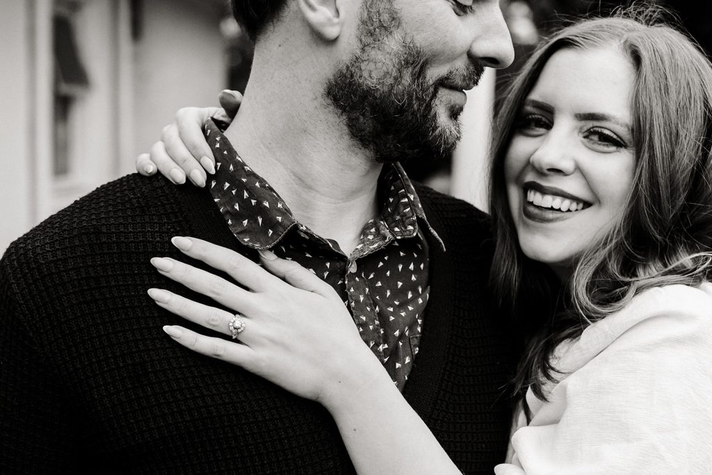 What to wear for my engagement session, cropped in photo of man looking at woman giving him a hug, showing off her ring by putting her hand on his chest