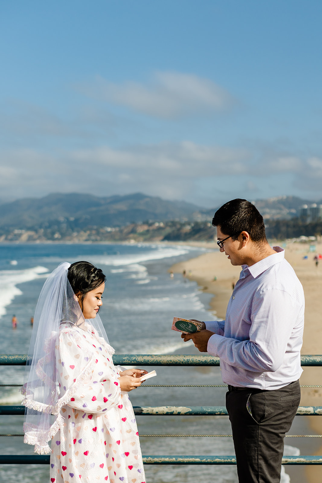 Couple exchanges vows on the pier, with a view of the coastline in the background during Santa Monica beach wedding. 
