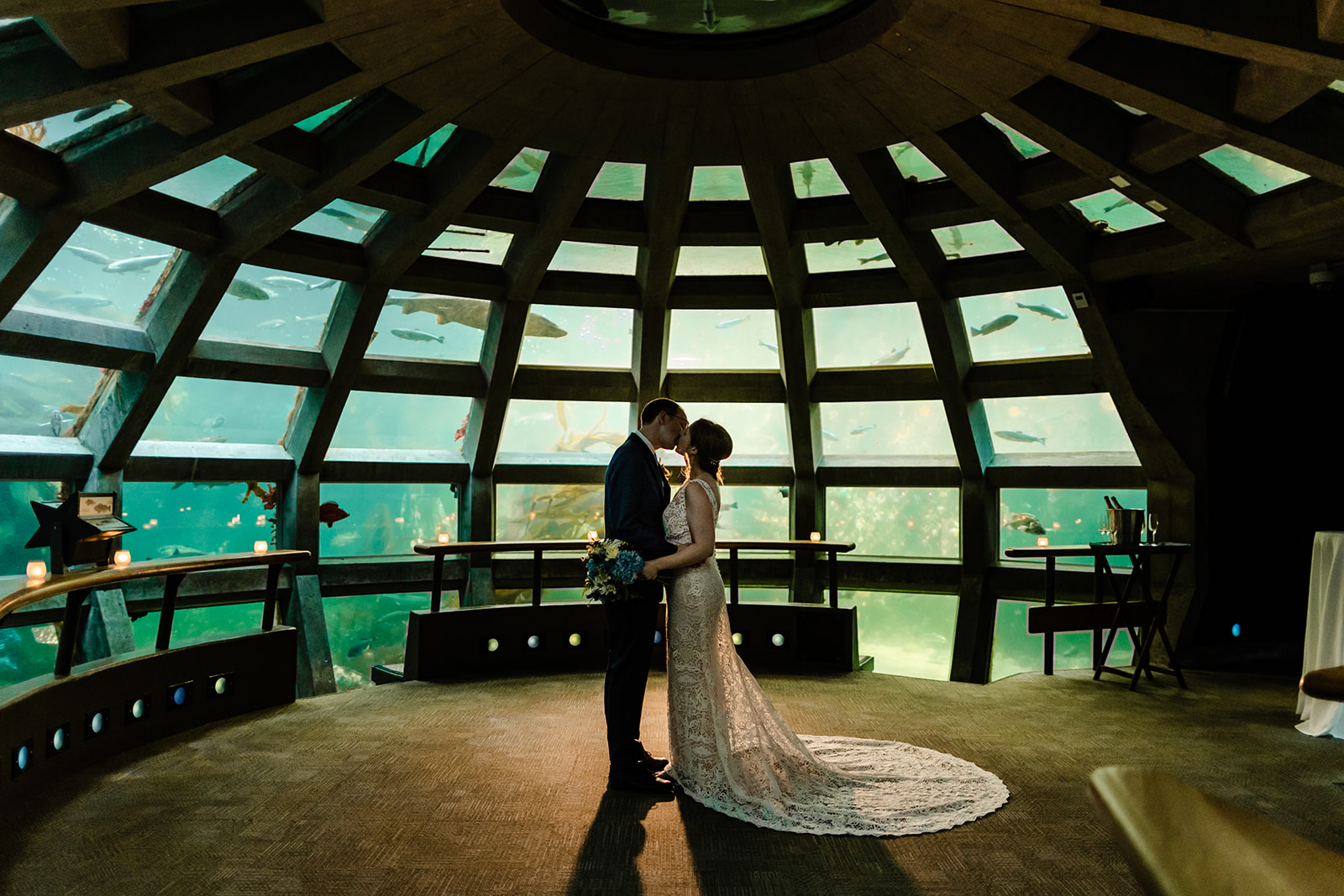 Couple embraces in a dome of the seattle aquarium, surrounded by fish.