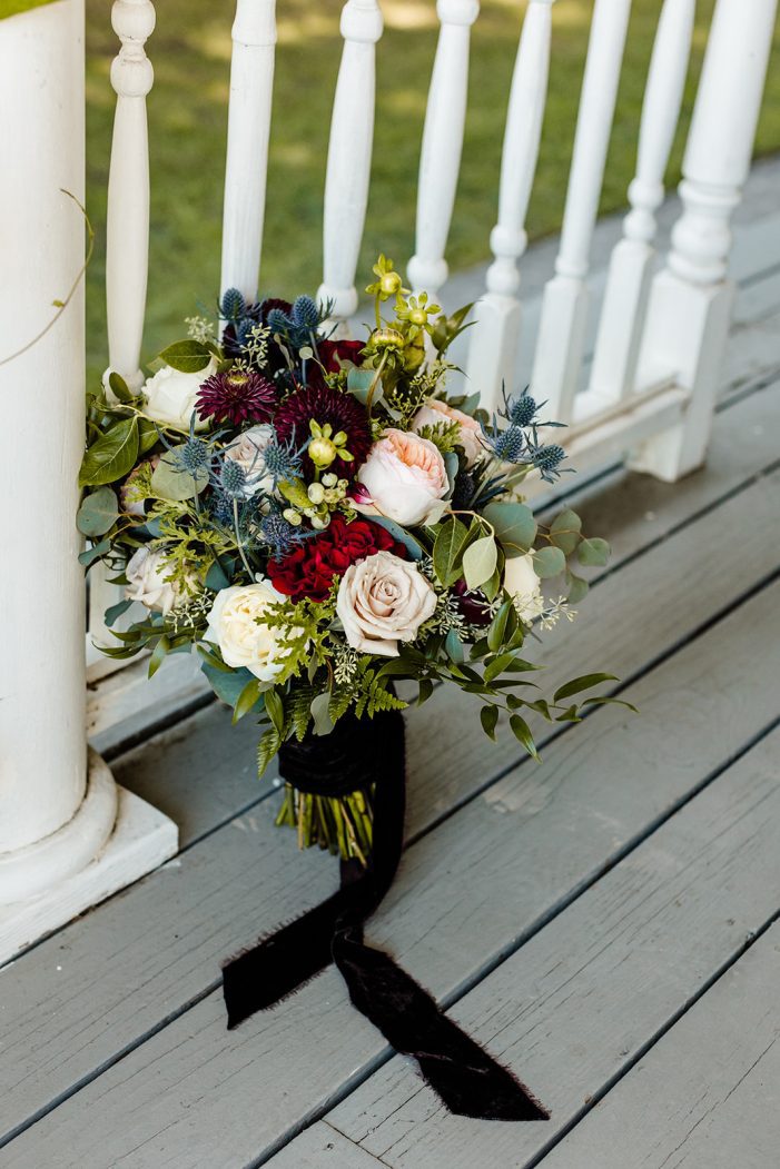 close up on bridal bouquet with blue, red, and white flowers, white roses, red dahlias