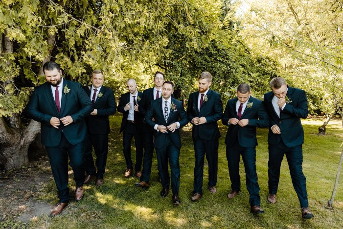 groom and groomsman walk while buttoning their dark blue suits