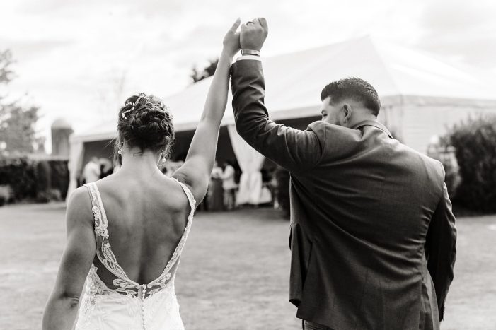 bride and groom walk towards large white tent holding arms in the air