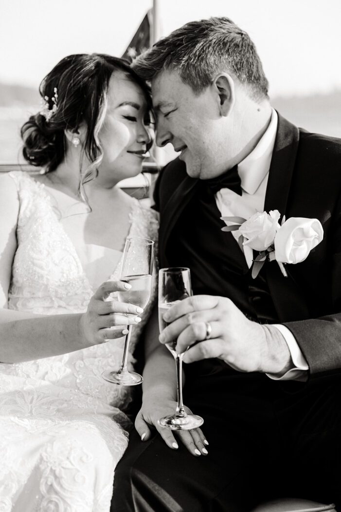 bride and groom hold champagne and snuggle in back of boat