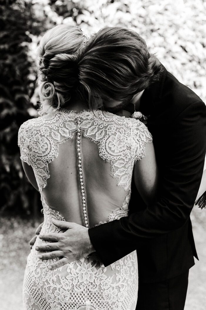 groom hugs bride, lace wedding dress details