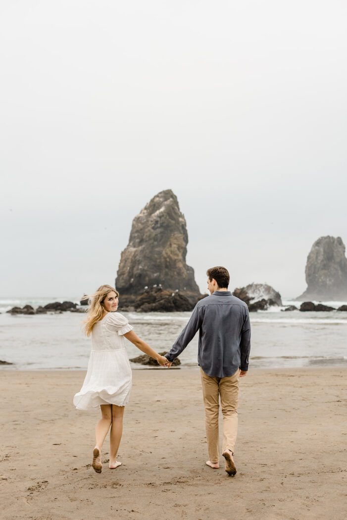 boy and girl hold hands as they walk towards the ocean