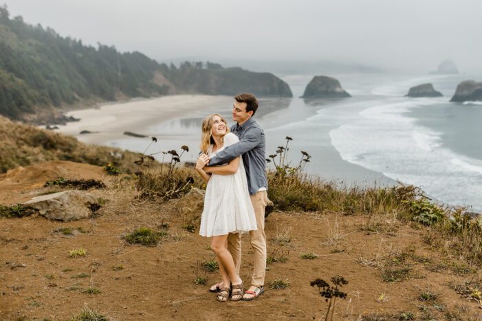 boy hugs girl from behind on cliff overlooking ocean