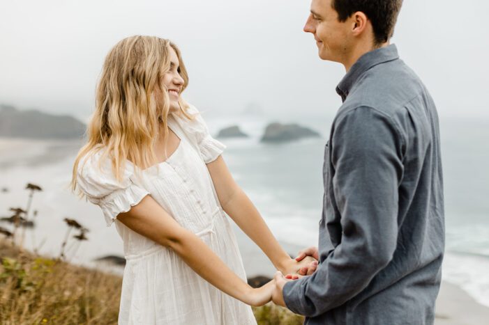 boy and girl hold hands with ocean behind them during engagement session at Cannon Beach