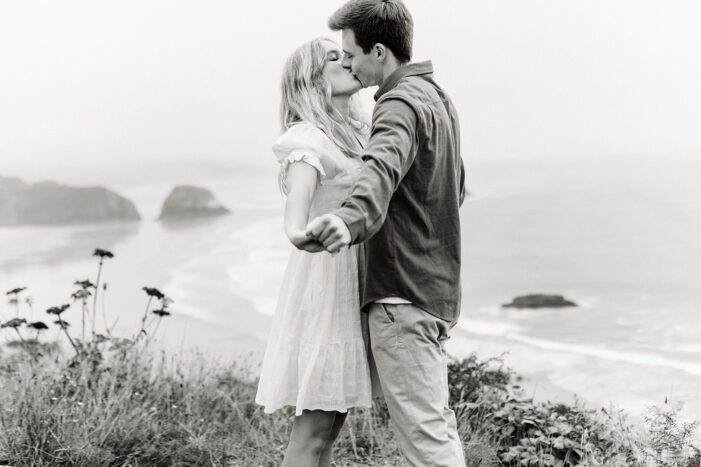 boy and girl hold hands and kiss with ocean behind them
