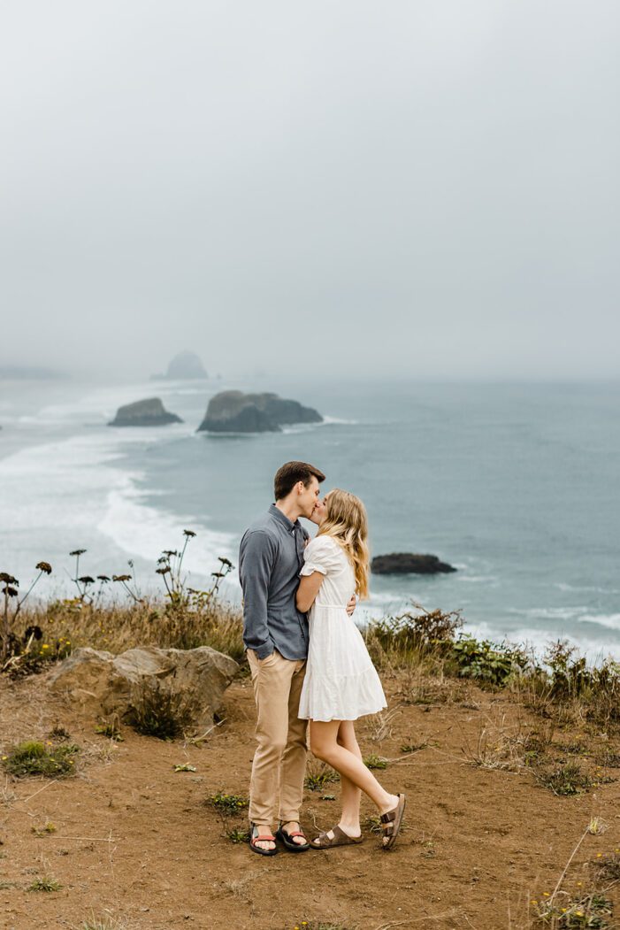 boy and girl kiss on cliffside during cannon beach engagement