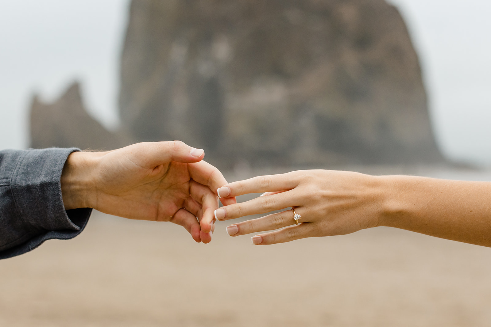 two hands reach for each other, one of them has a diamond engagement ring
