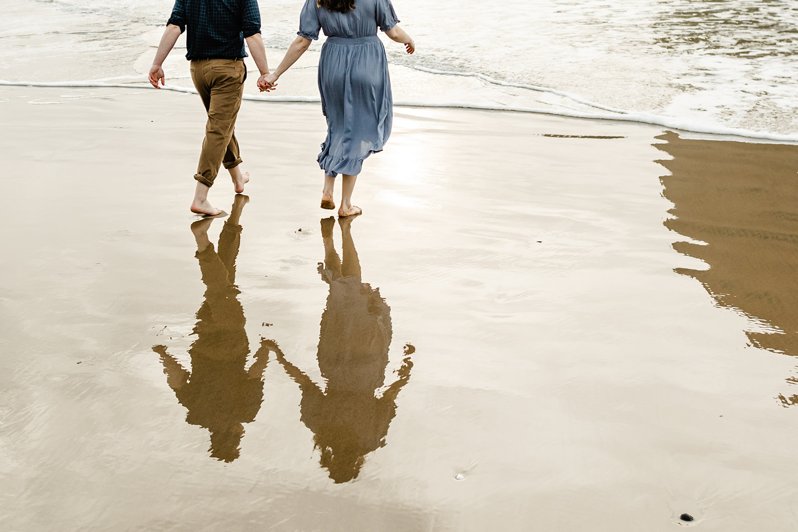 boy and girl walk into the ocean with their shadows in the water behind them