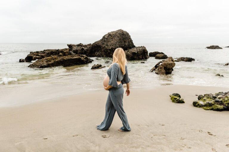 pregnant woman walks on beach staring out to the ocean laguna beach maternity shoot