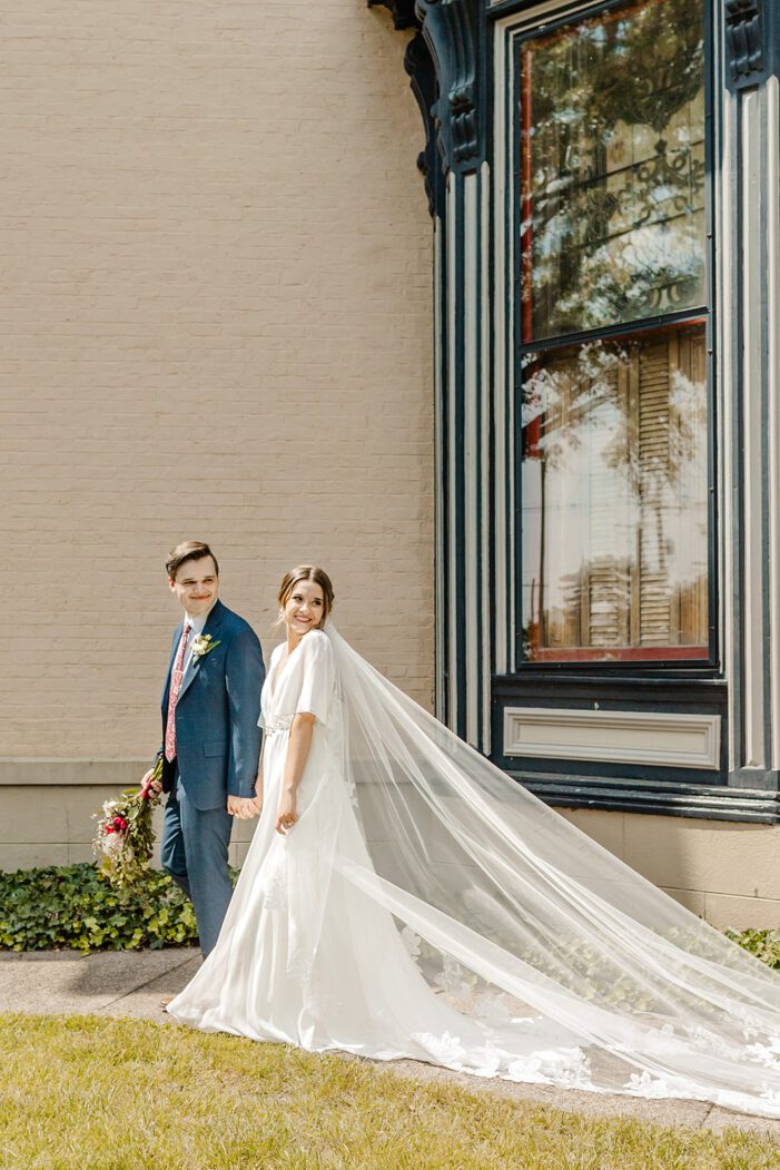bride and groom walk while veil trails behind bride