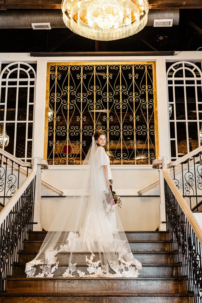 bride stands at top of stairs with veil trailing behind her