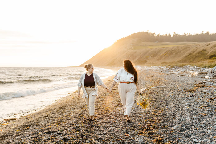 two women walk down beach holding hands during Whidbey Island Engagement