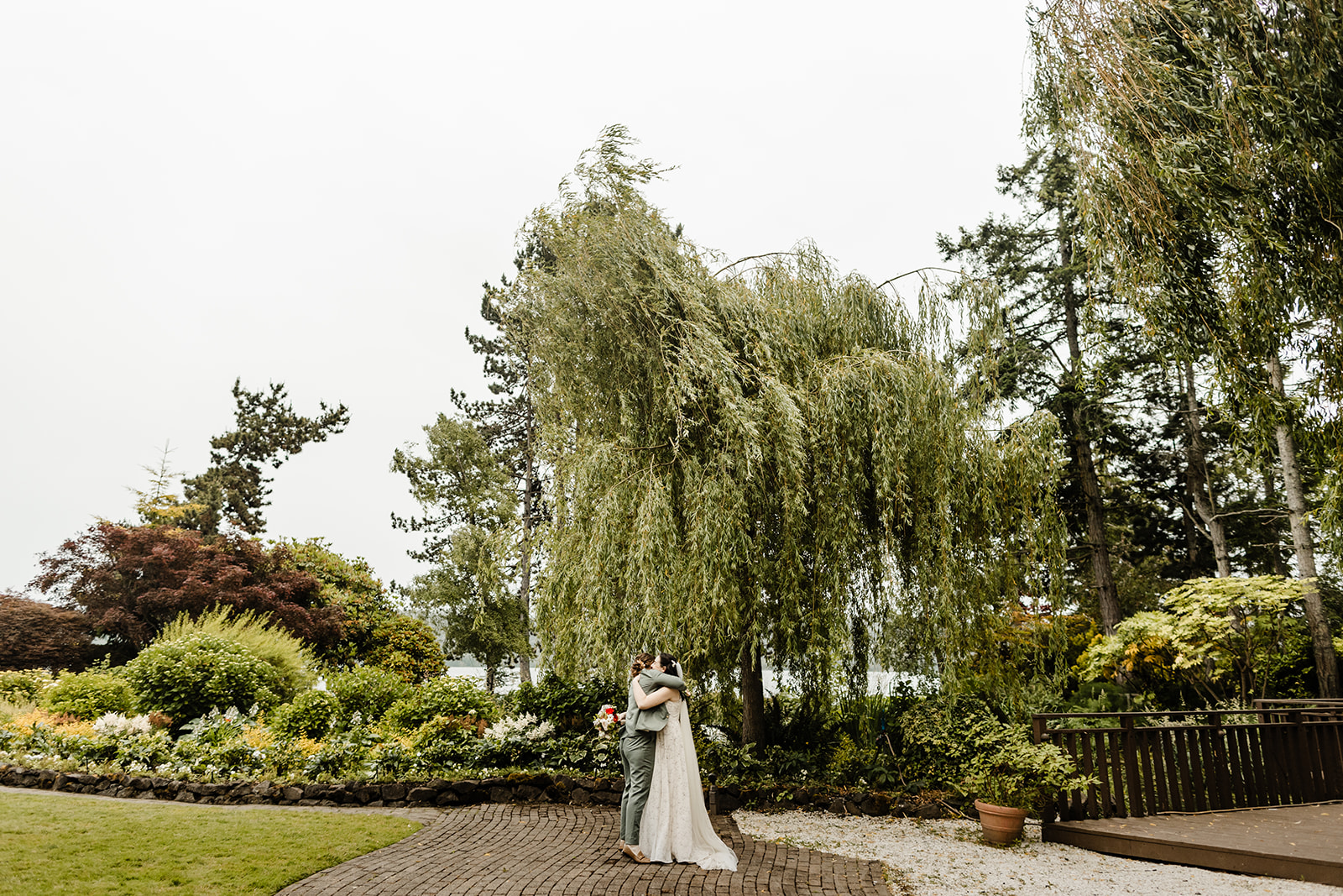 two brides huddle together under a willow tree