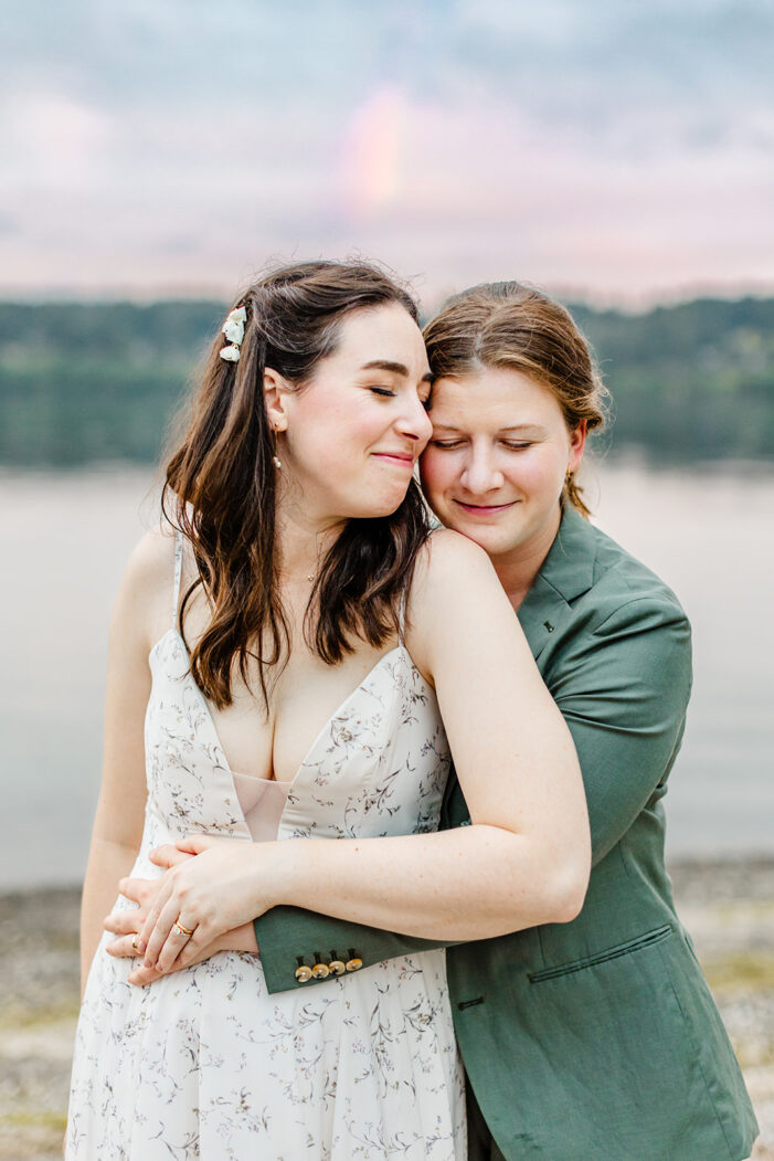 two brides cuddle in front of water