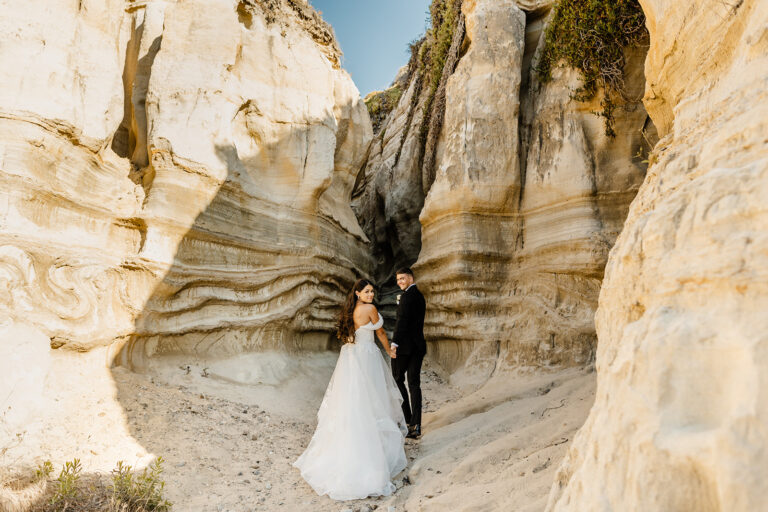 bride and groom hold hands and walk together towards a crevice in a rock wall