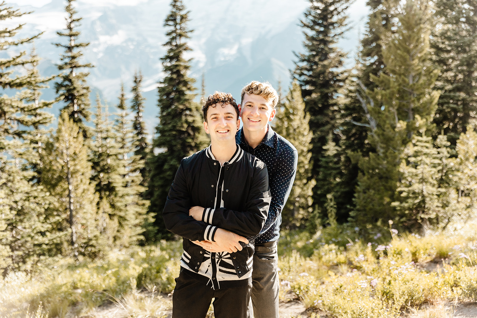 one boy hugs another boy from behind as they pose in the woods