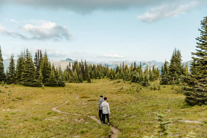 two boys walk across a hill in a field during mt rainier engagement session