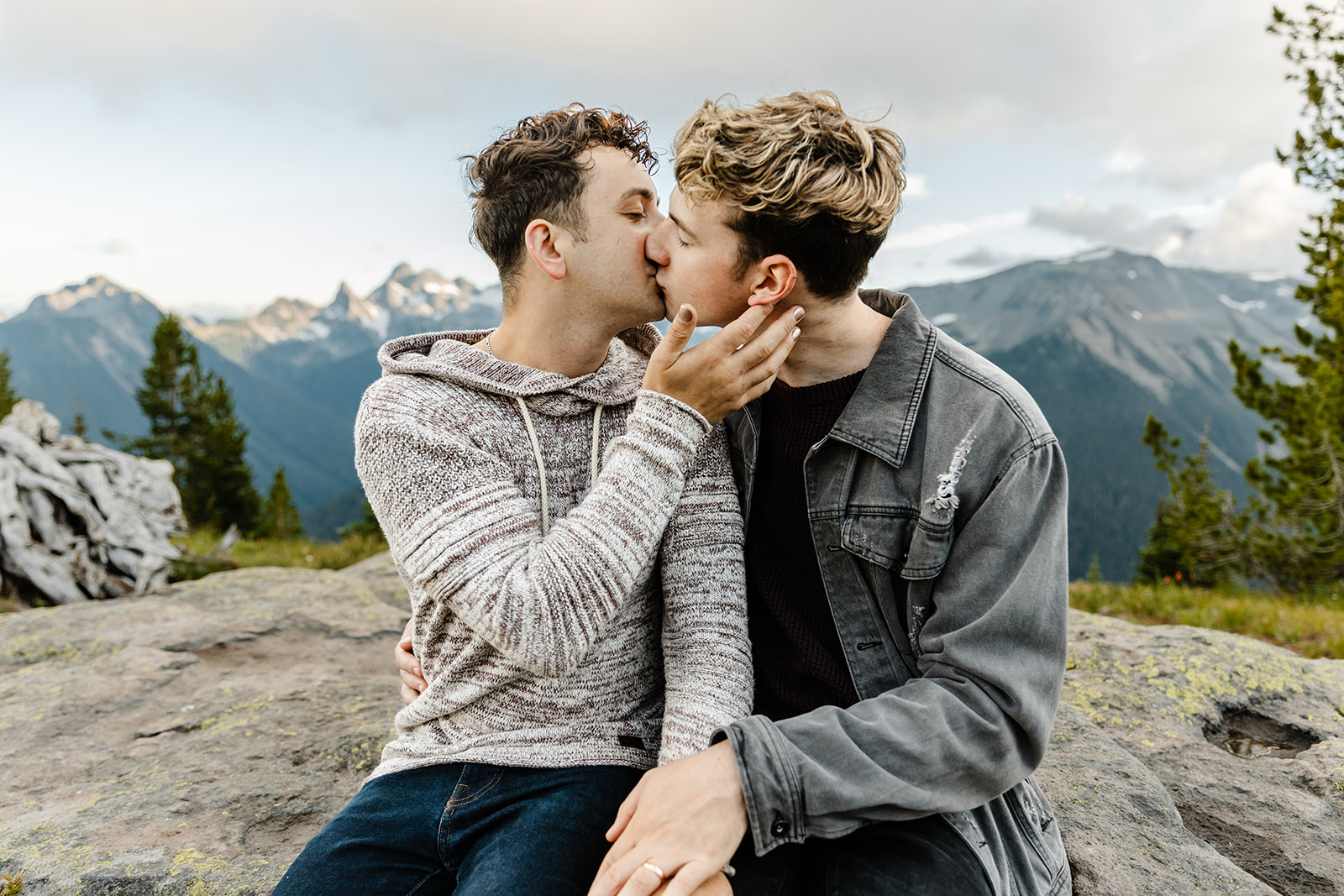 two boys kiss while sitting on a rock together