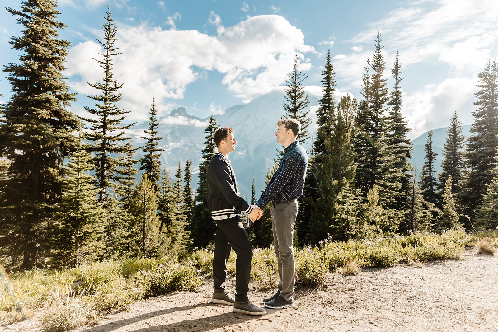 two boys stand facing each other, holding hands with mountains and trees around them