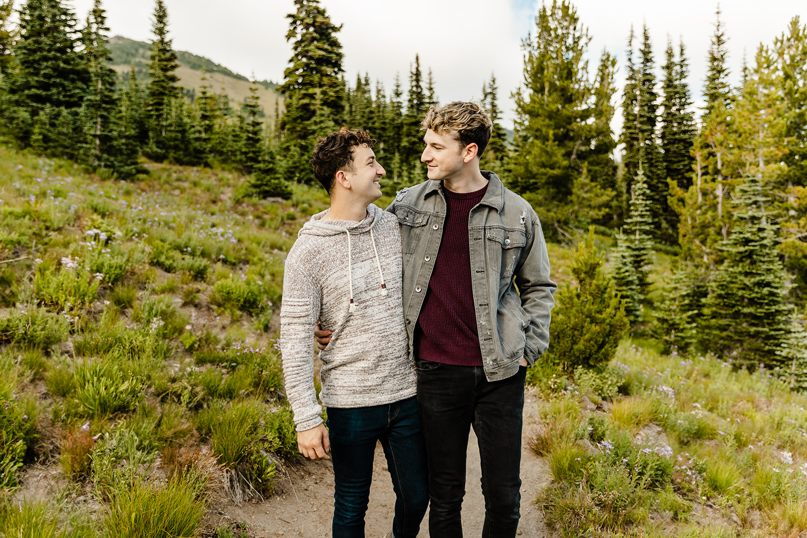 two boys look at each other  with field and trees around them during mt rainier engagement session