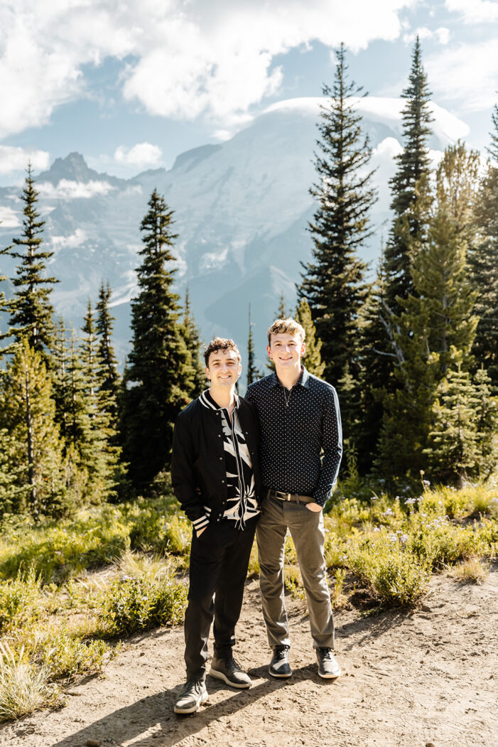 two boys stand and smile  surrounded by trees and mountains