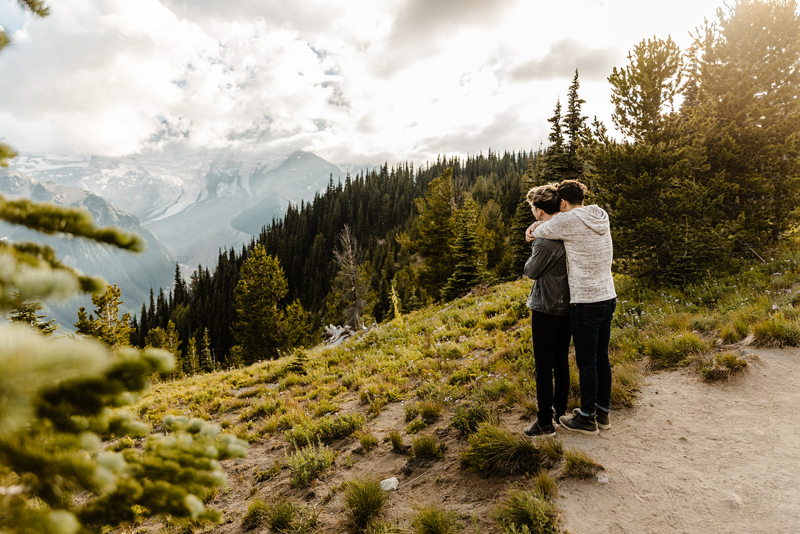 one boy hugs another from behind as they look out over the wilderness