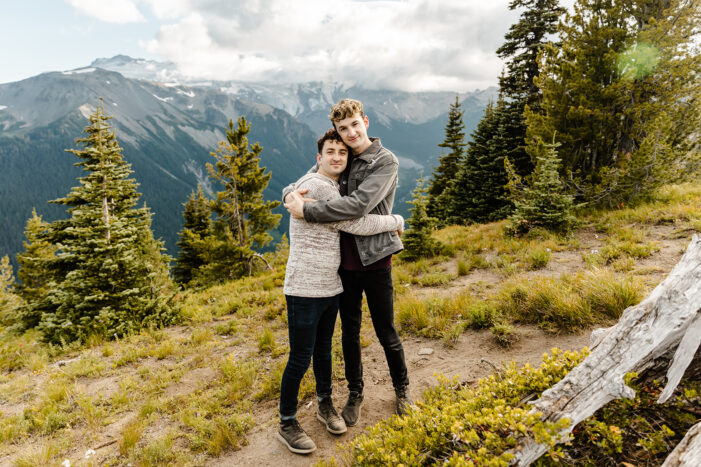 two boys walk down a path through a field with trees in the background